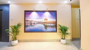 A framed painting of a cityscape with a tower, mounted on a wall in a hallway with two potted plants. - Fabhotel Prime Familto (Baruipur)