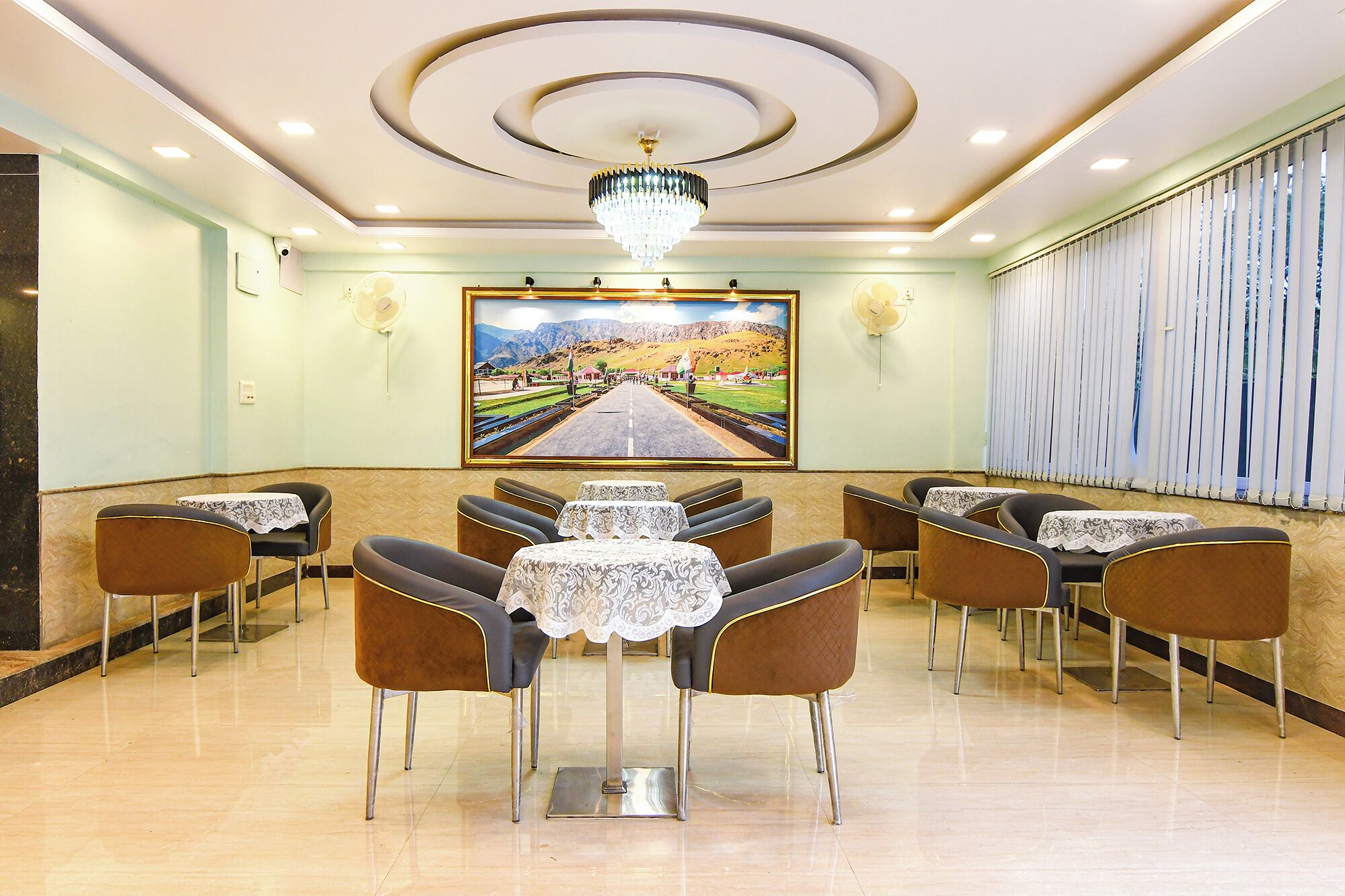 A dining area with a central table, surrounded by chairs, and a large landscape painting on the wall.