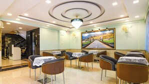 A restaurant with a modern interior, featuring a chandelier, a large landscape painting on the wall, and several tables and chairs. - Fabhotel Prime Familto (Baruipur)