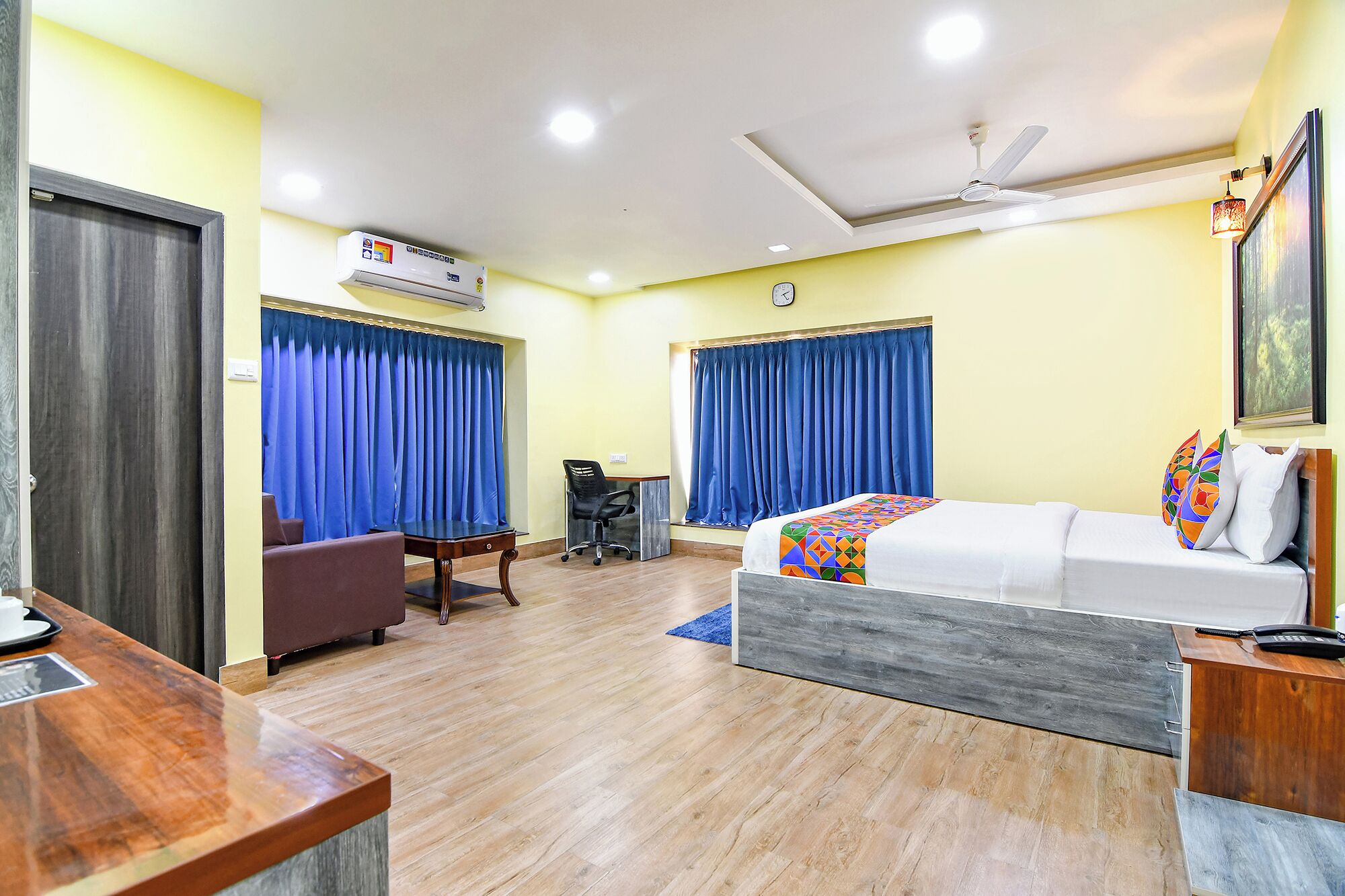 Una habitación de hotel con cama, escritorio, silla, equipo de aire acondicionado y ventilador de techo.