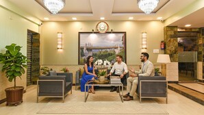 A lobby with a reception desk, two grey armchairs, a coffee table, and a chandelier. - Fabhotel Prime Familto (Baruipur)