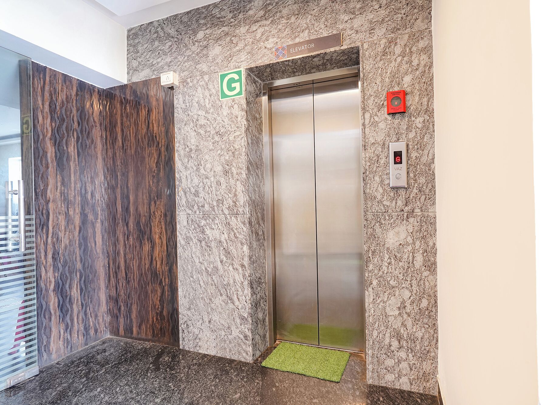 An elevator with a marble wall, a green sign, and a red emergency button.