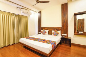 Ein Hotelzimmer mit Bett, Vorhängen, Deckenventilator, Klimaanlage, Nachttisch und Spiegel.