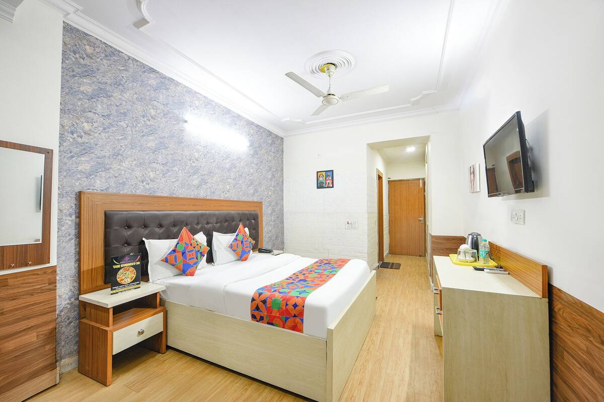 A hotel room with a bed, bedside table, TV, and a bathroom visible through an open door.