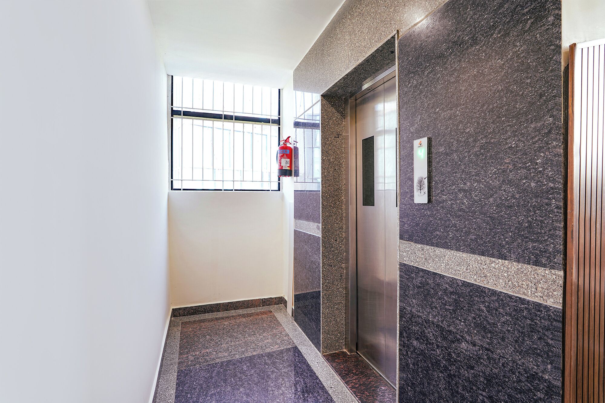 A hallway with a fire extinguisher, an elevator, and a wall with a textured pattern.
