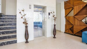 Eine moderne Lobby mit Marmorstufen, zwei dekorativen Vasen, einer Holzwand mit geometrischem Muster und einem blauen Sofa.