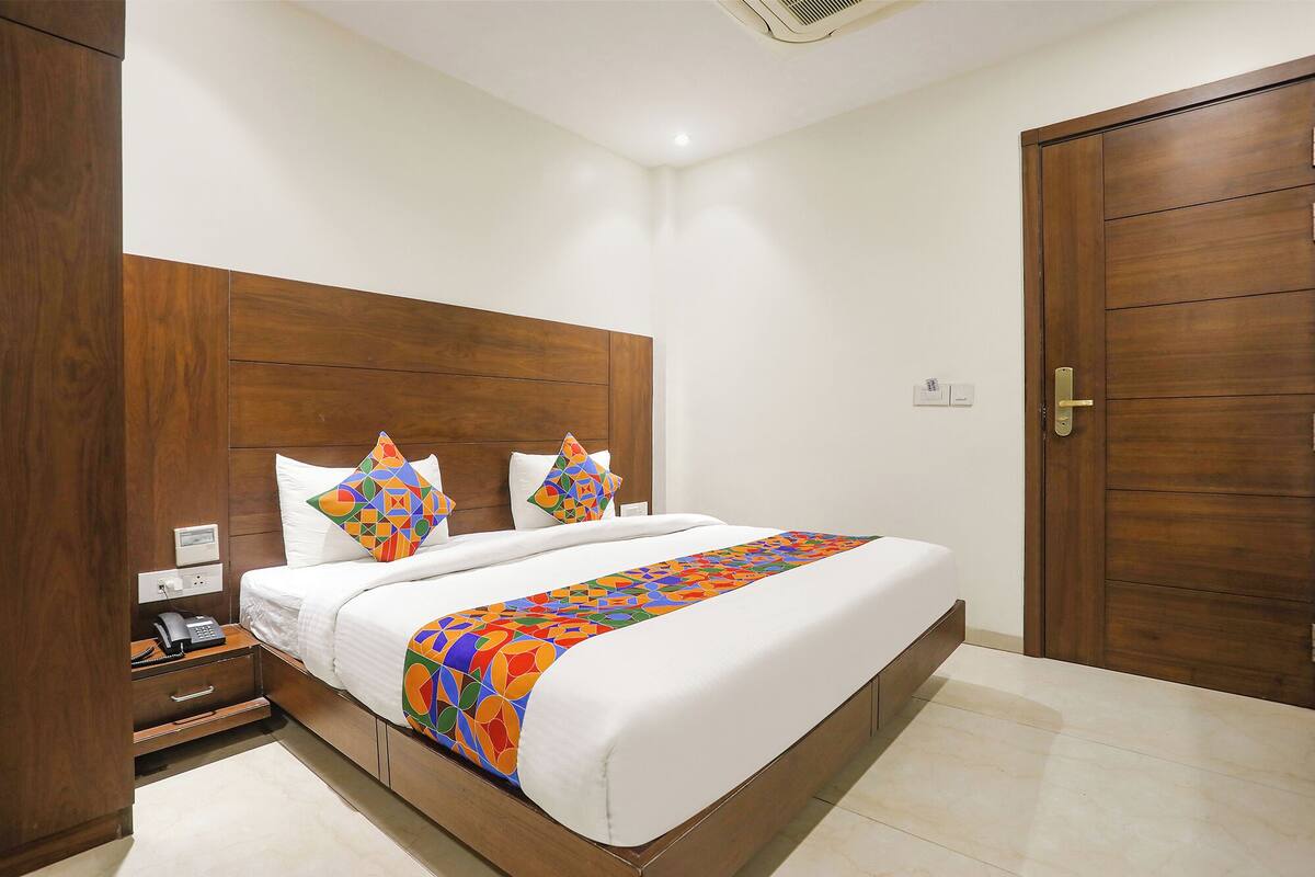 A neatly made bed with a colorful geometric-patterned throw, a wooden headboard, and a bedside table with a telephone.