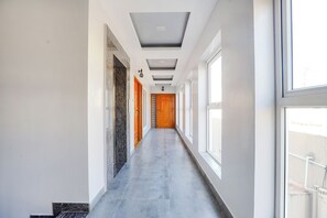 Ein langer, schmaler Korridor mit einer Marmorwand auf einer Seite und einem Fenster auf der anderen. Am Ende des Ganges befinden sich Türen.
