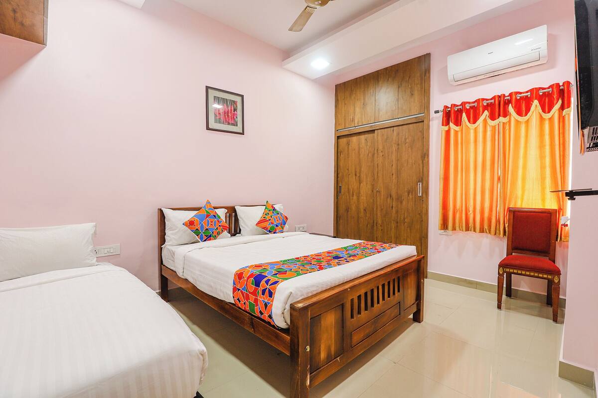 A bedroom with a wooden bed, a wooden wardrobe, a red chair, and a window with orange curtains.