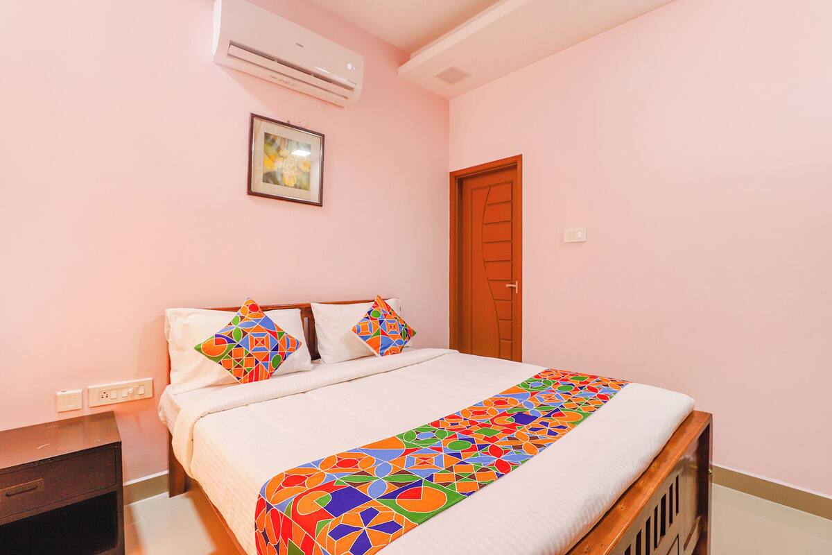 A bedroom with a bed, a wooden headboard, a wall-mounted air conditioner, a framed picture, and a door.