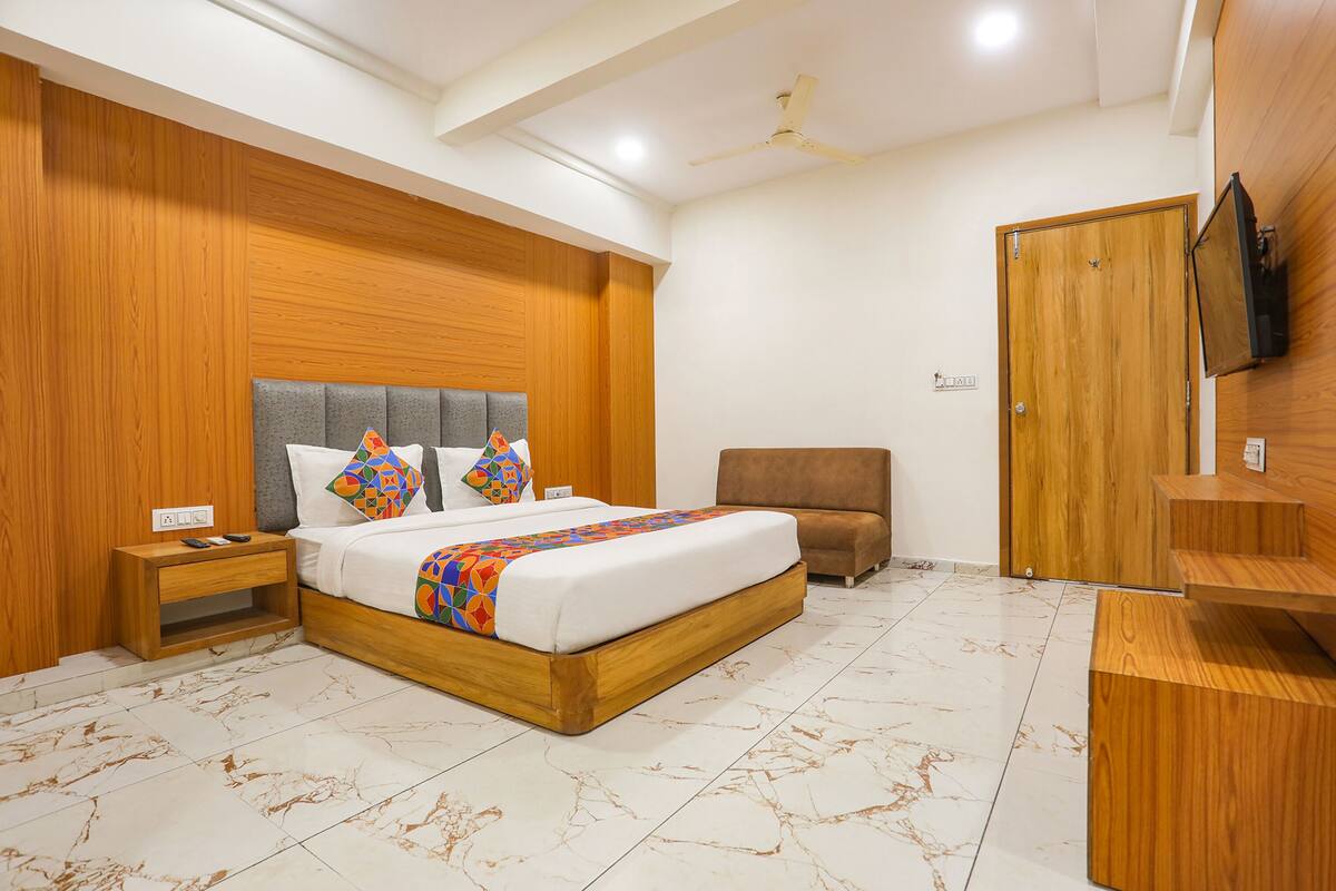 A modern bedroom with a wooden headboard, a bed with colorful bedding, a nightstand, a brown armchair, a wooden wardrobe, and a ceiling fan.