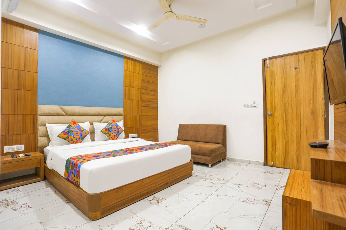A bedroom with a bed, bedside table, nightstand, wooden wardrobe, and a TV.