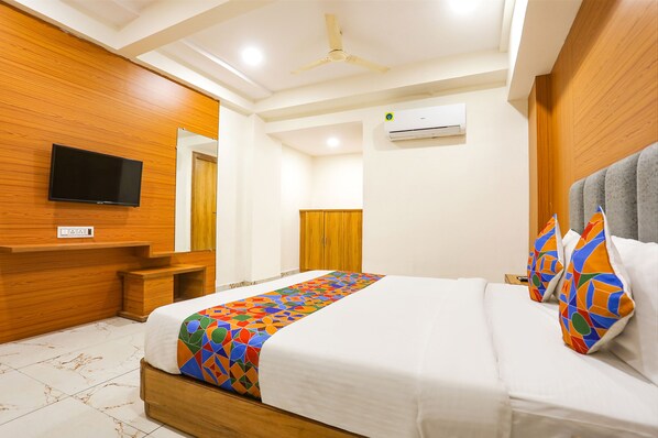 A hotel room with a bed, a television, a wardrobe, and an air conditioning unit.