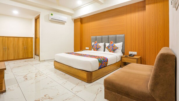 A bedroom with a bed, bedside table, and a brown chair. - Fabhotel Raj Villa (Gandhinagar)