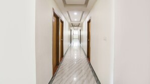 A long, narrow hallway with a marble floor and wooden doors on both sides. - Fabhotel Raj Villa (Gandhinagar)