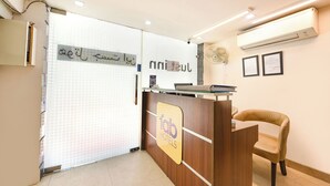 A hotel reception area with a wooden reception desk, a single chair, and a tiled wall with Arabic text. - Fabhotel Just Inn (New Delhi)