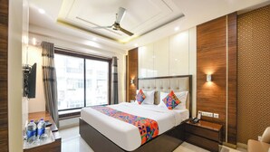 A modern hotel room with a large bed, a ceiling fan, a desk with a telephone, and a window with curtains. - Fabhotel Just Inn (New Delhi)