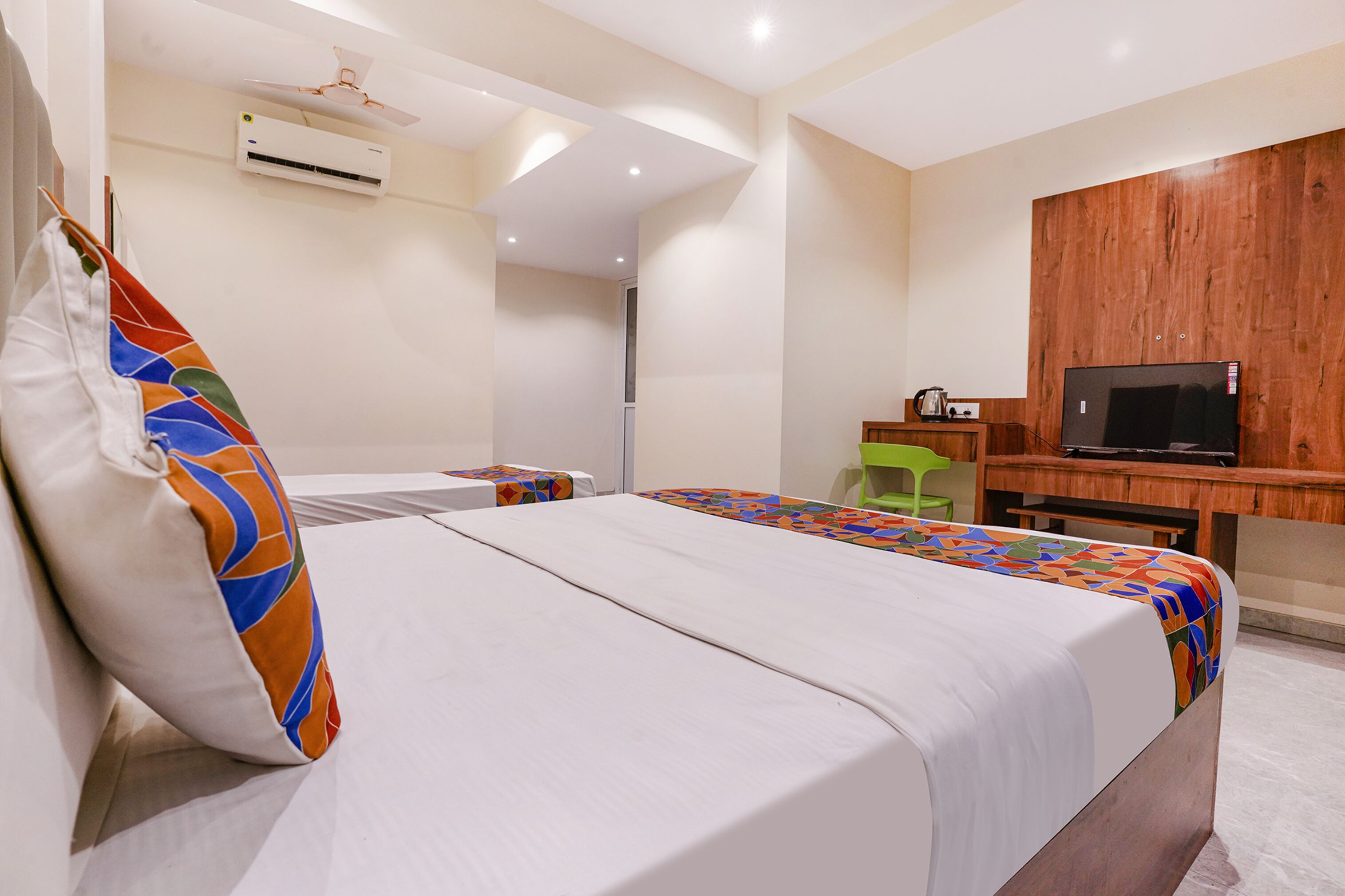 Una habitación de hotel con cama, escritorio, silla, televisor y aire acondicionado.