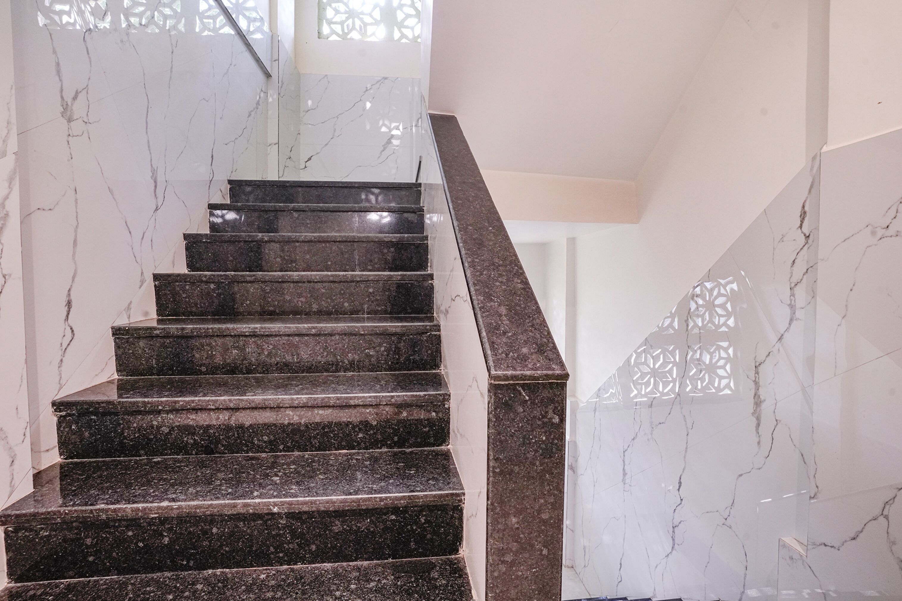 Un escalier en marbre, doté d’une rampe, mène à une pièce dont le mur est blanc et qui est agrémentée d’une grille décorative sur la fenêtre.