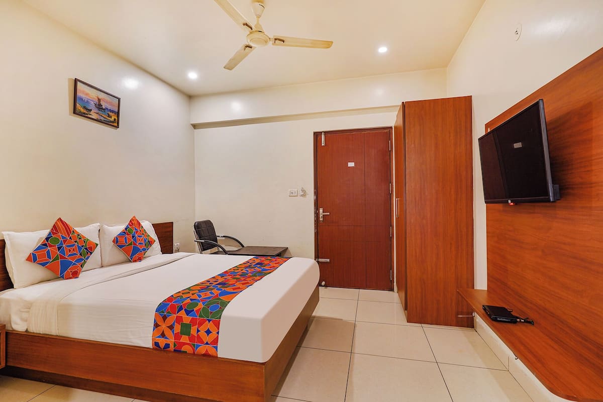 A hotel room with a bed, a desk, a chair, a television, and a door.