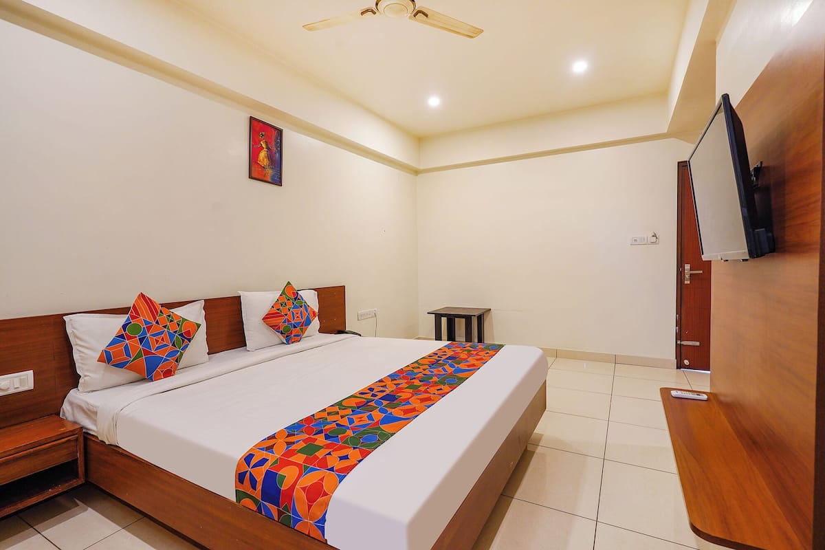 A hotel room with a bed, a wooden headboard, a small table, a TV, and a ceiling fan.
