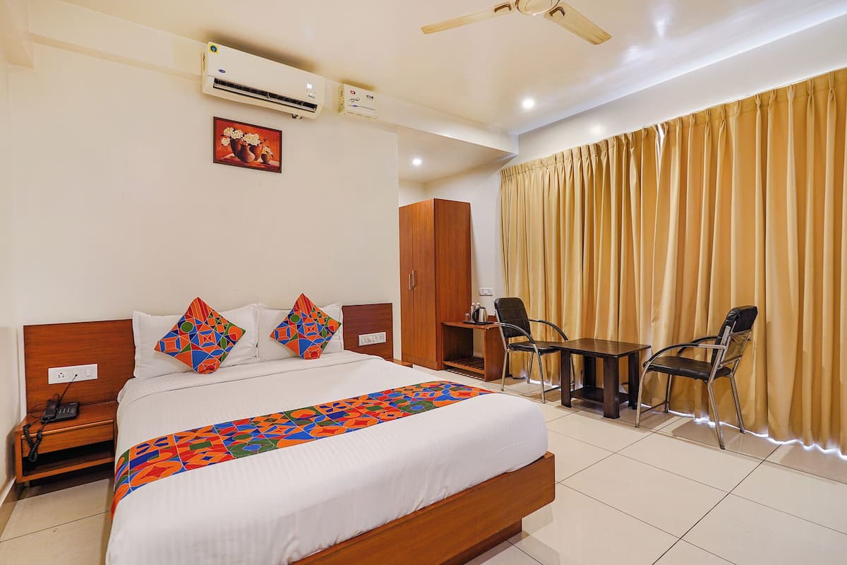 A hotel room with a bed, a desk, a chair, a wardrobe, and an air conditioning unit.