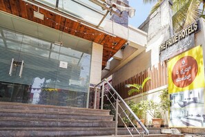 A hotel entrance with a staircase leading up to a wooden door, a metal railing, and a large signboard with text. - FabHotel The Prime - Near HRBR Layout, Horamavu (Bengaluru)