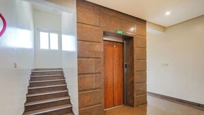 Um corredor com elevador de madeira, escada e parede com textura.