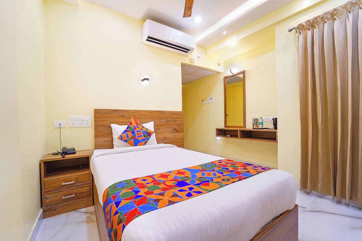 A hotel room with a bed, a nightstand, a mirror, and a window with curtains.