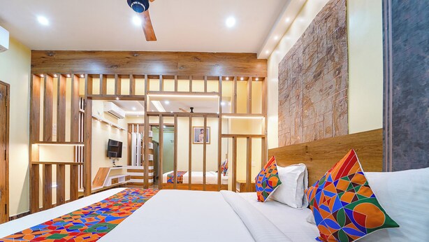A modern hotel room with a large bed, colorful pillows, a wooden headboard, and a decorative wall panel. - Fabhotel Ink (Coimbatore)