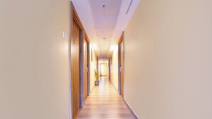 A long, narrow hotel corridor with wooden doors on both sides, a wooden floor, and a ceiling with recessed lighting. - Fabhotel Ink (Coimbatore)