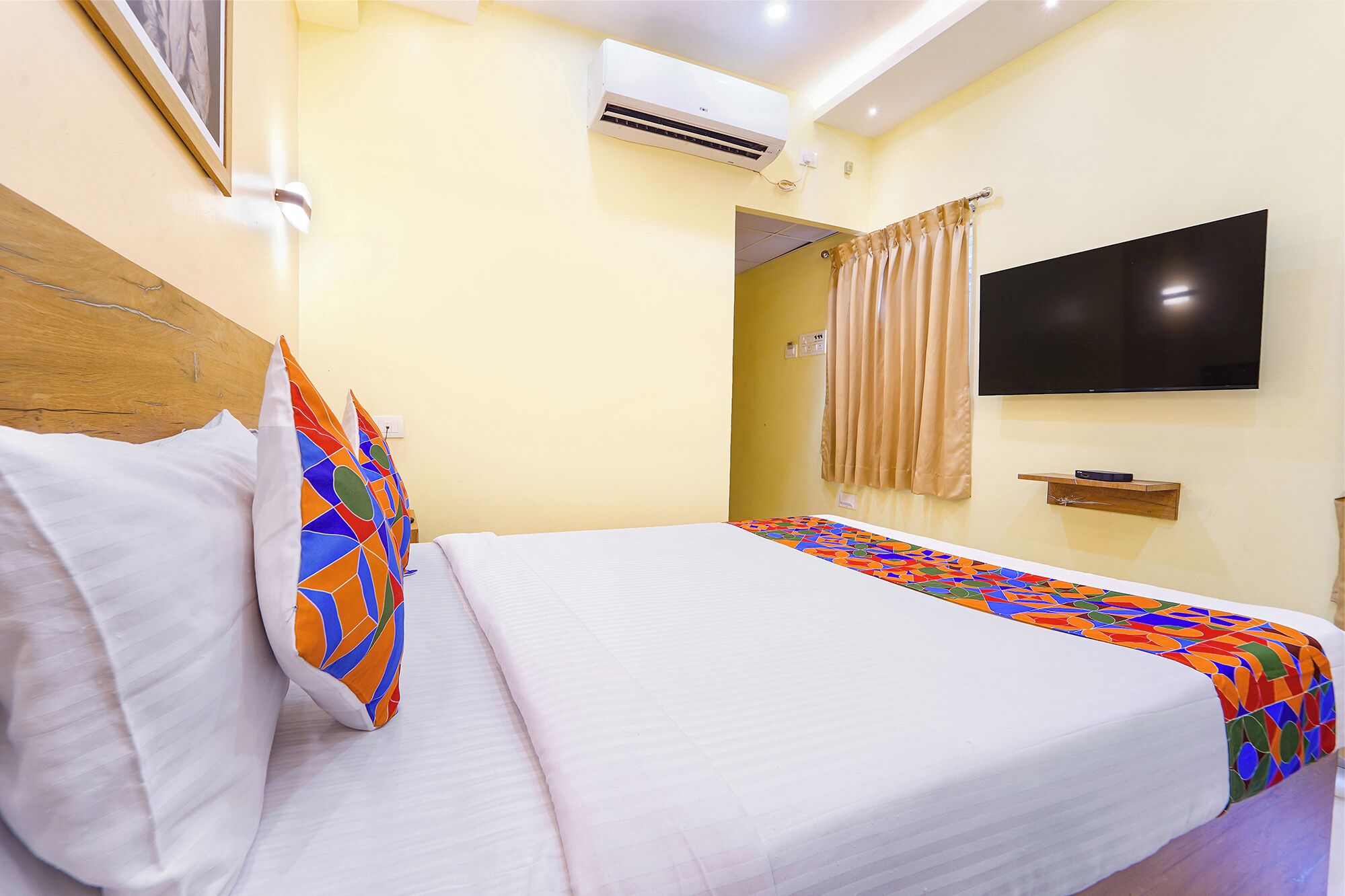 A hotel room with a bed, a television, and an air conditioning unit.
