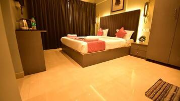 A modern bedroom with a large bed, a bedside table, a nightstand, and a small desk with a lamp.