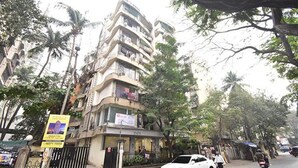A multi-story building with balconies, a gated entrance, and a signboard.