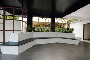 A modern interior with a curved white bench, dark flooring, and a view of greenery outside. - Fabhotel The Botanica (Hyderabad)
