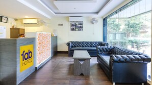 A hotel lobby with a reception desk, a sofa, a coffee table, and a large window offering a view of the outdoors. - Fabhotel Shalom Indus Residency (Candolim)