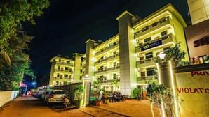 A multi-story hotel with balconies, a well-lit entrance, and a paved driveway. - Fabhotel Shalom Indus Residency (Candolim)