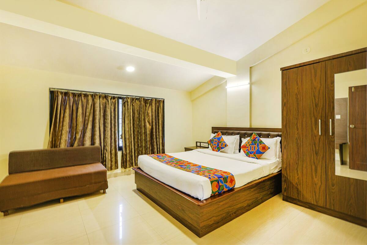 A hotel room with a bed, a sofa, a wardrobe, and a window with curtains.