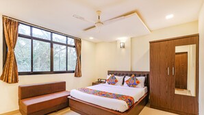 A bedroom with a bed, a wooden wardrobe, a bench, a ceiling fan, and a window with curtains. - Fabhotel Shalom Indus Residency (Candolim)