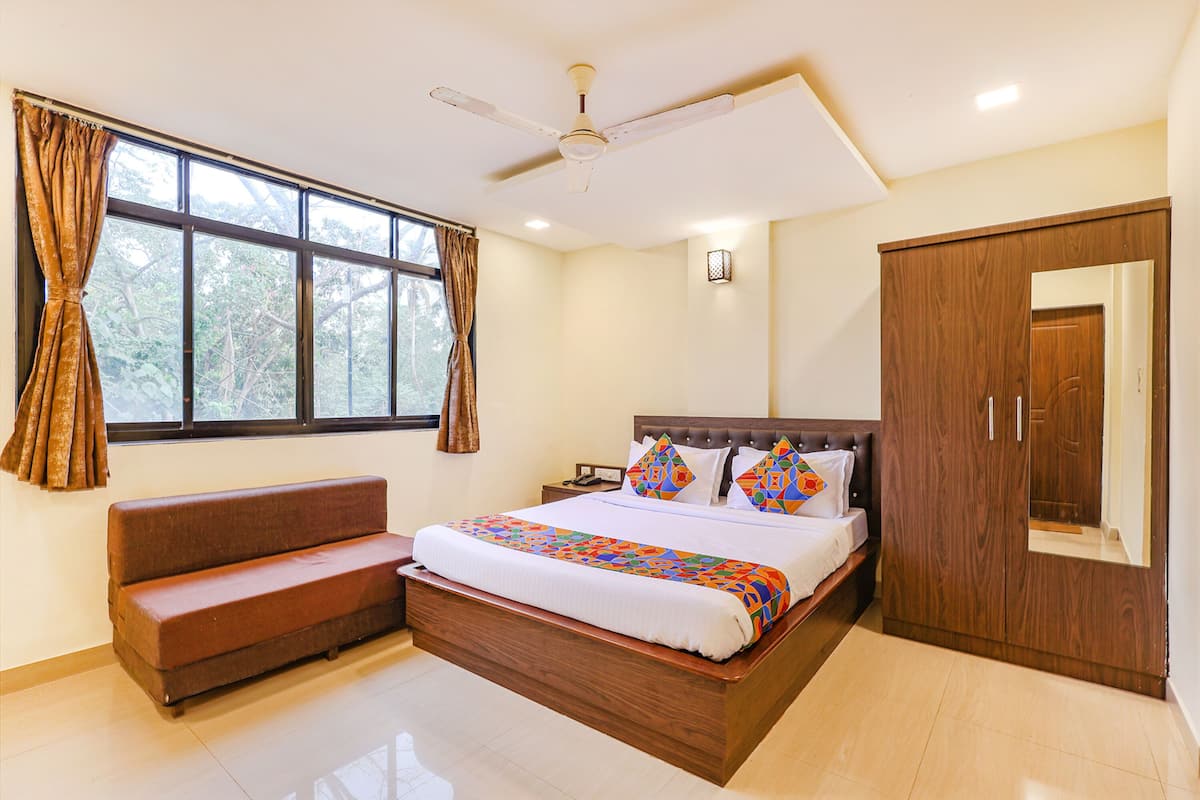A bedroom with a bed, a wooden wardrobe, a bench, a ceiling fan, and a window with curtains.