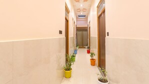 A hallway with a marble floor, potted plants, and a ceiling with geometric patterns. - Fabhotel Hridyam Madhuram (Faizabad)