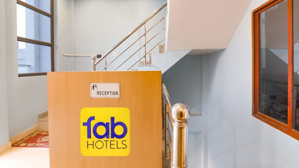 A reception desk with a sign for Fab Hotels, a staircase, and a window with a view. - Fabhotel Hridyam Madhuram (Faizabad)