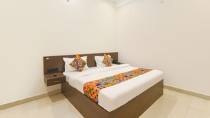 A neatly made bed with a patterned bedspread, a wooden headboard, and a bedside table with a drawer. - Fabhotel Hridyam Madhuram (Faizabad)