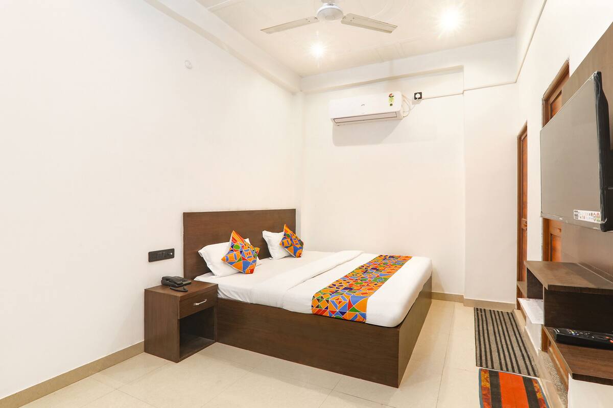 Habitación de hotel con cama, mesita de noche, ventilador de techo, aire acondicionado y televisión.