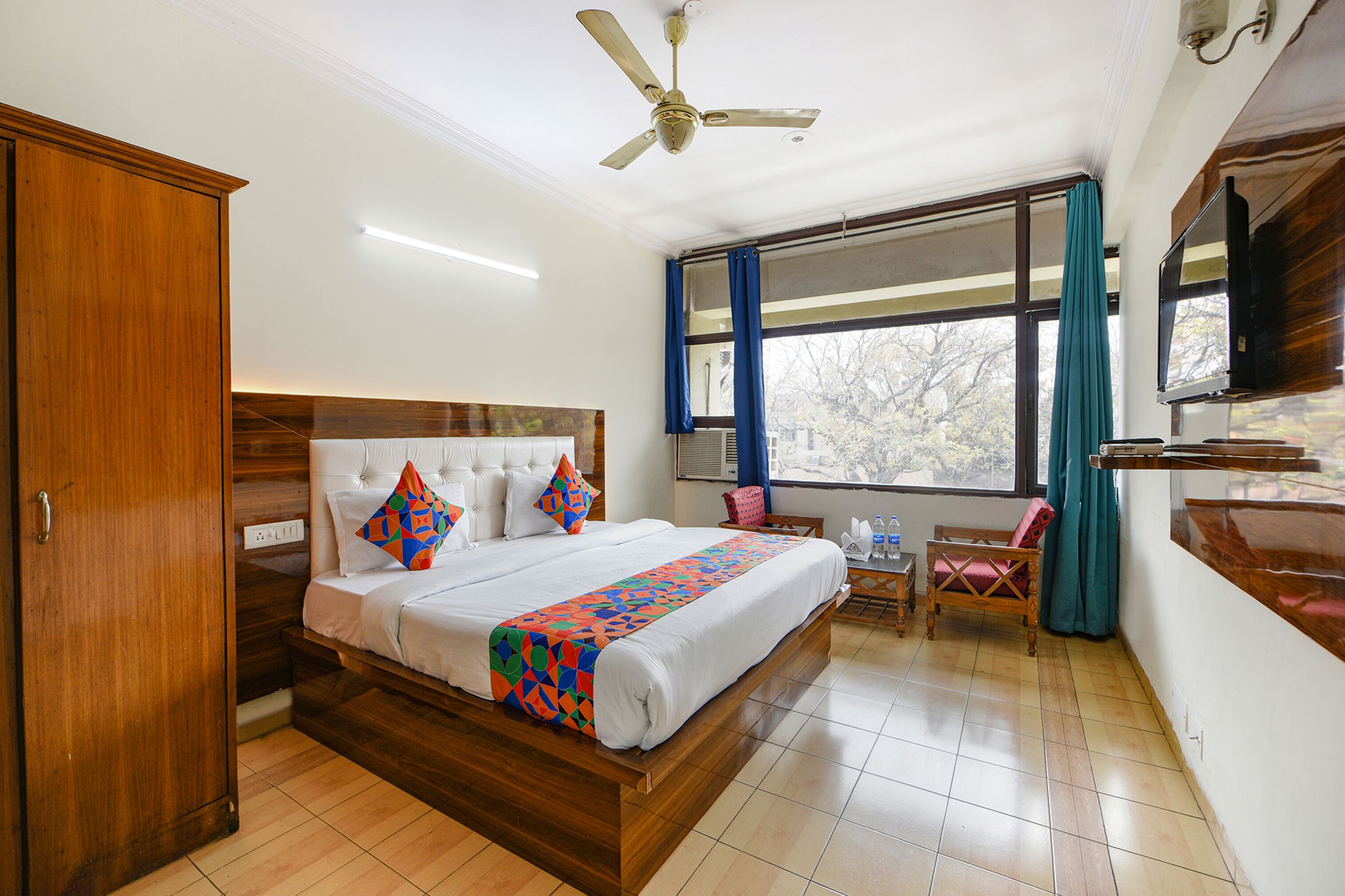 A bedroom with a wooden bed, a ceiling fan, a TV, and a window with curtains.