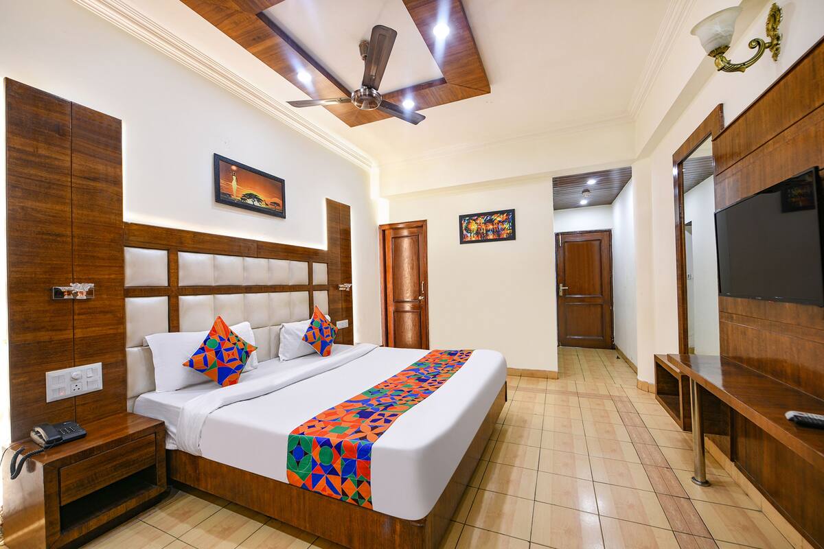 A hotel room with a bed, wooden headboard, a ceiling fan, a nightstand, a TV, and a bathroom door.