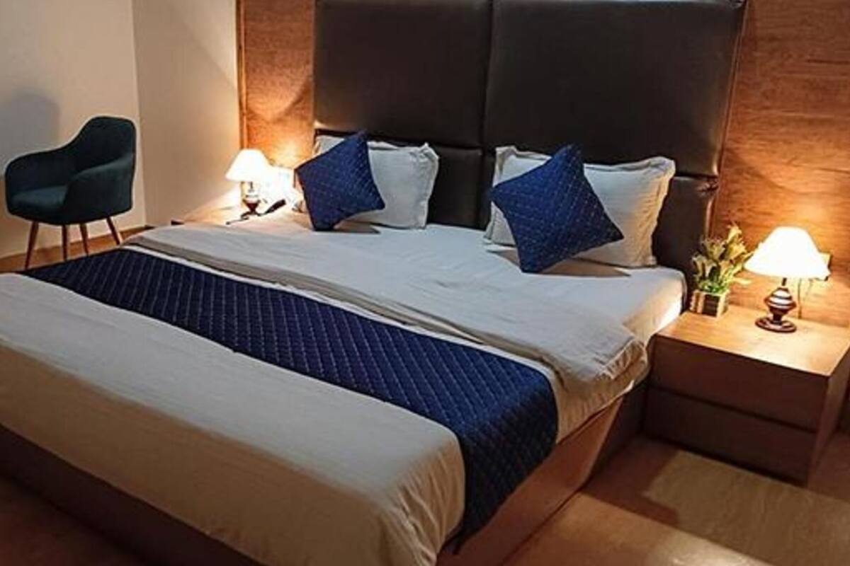 A double bed with a dark blue quilt, two bedside tables with lamps, a dark headboard, and a small round table with a vase of flowers.