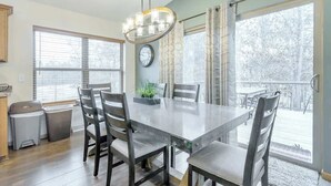 A dining area with a large table and chairs, a chandelier, and a view through large windows.