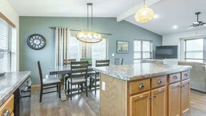 A kitchen with a dining area, wooden cabinets, a large island, and a TV in the living room.