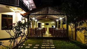 An outdoor covered seating area with chairs arranged for guests, a pathway leading to the entrance, and a building with a balcony in the background. - Mamma Raji Hotel (Negombo)